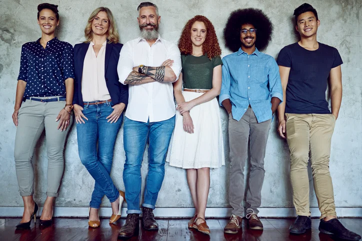 Six diverse people standing side by side against a concrete wall, smiling